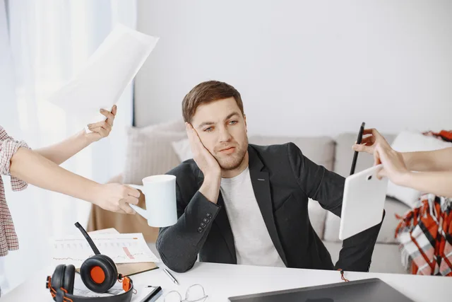 A businessman overwhelmed by tasks in a modern office setting, depicting multitasking and stress. Leistungsumfang und Abgrenzung bei Agenturverträgen verstehen